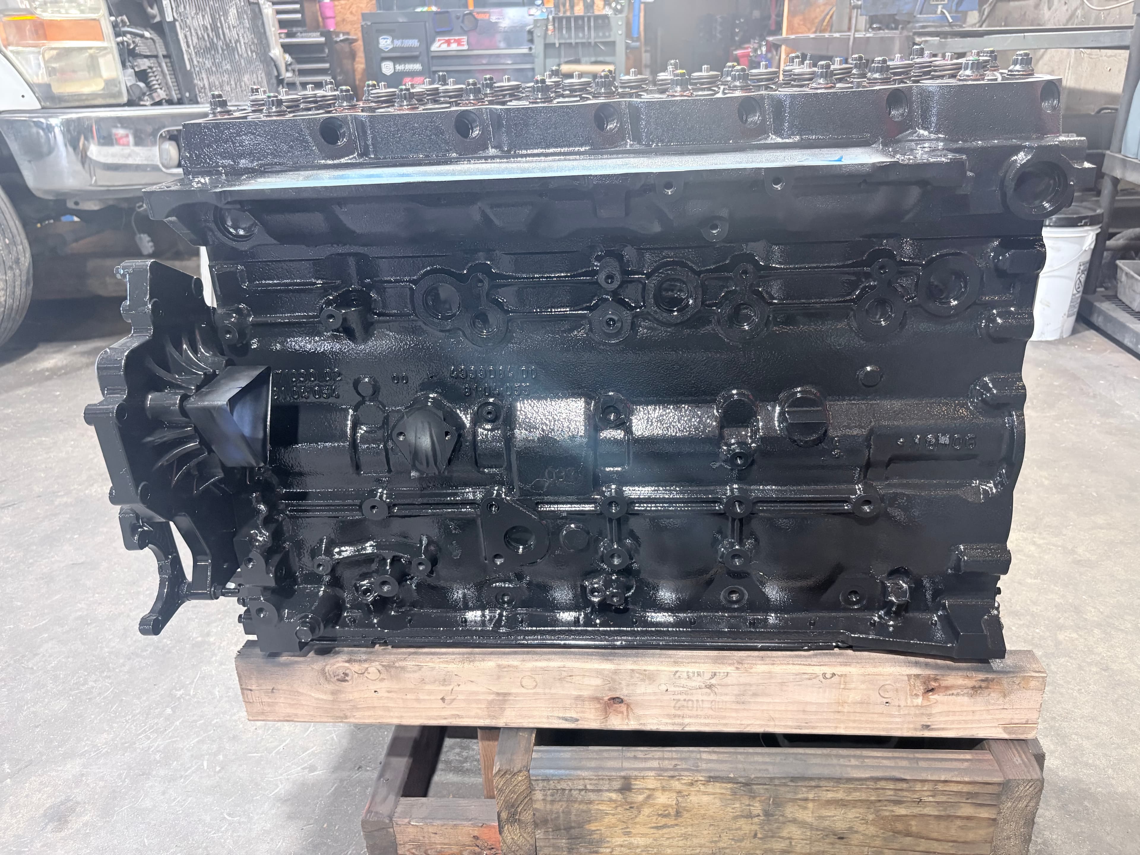 Freshly painted glossy black engine block resting on a wooden pallet in a mechanic's workshop.