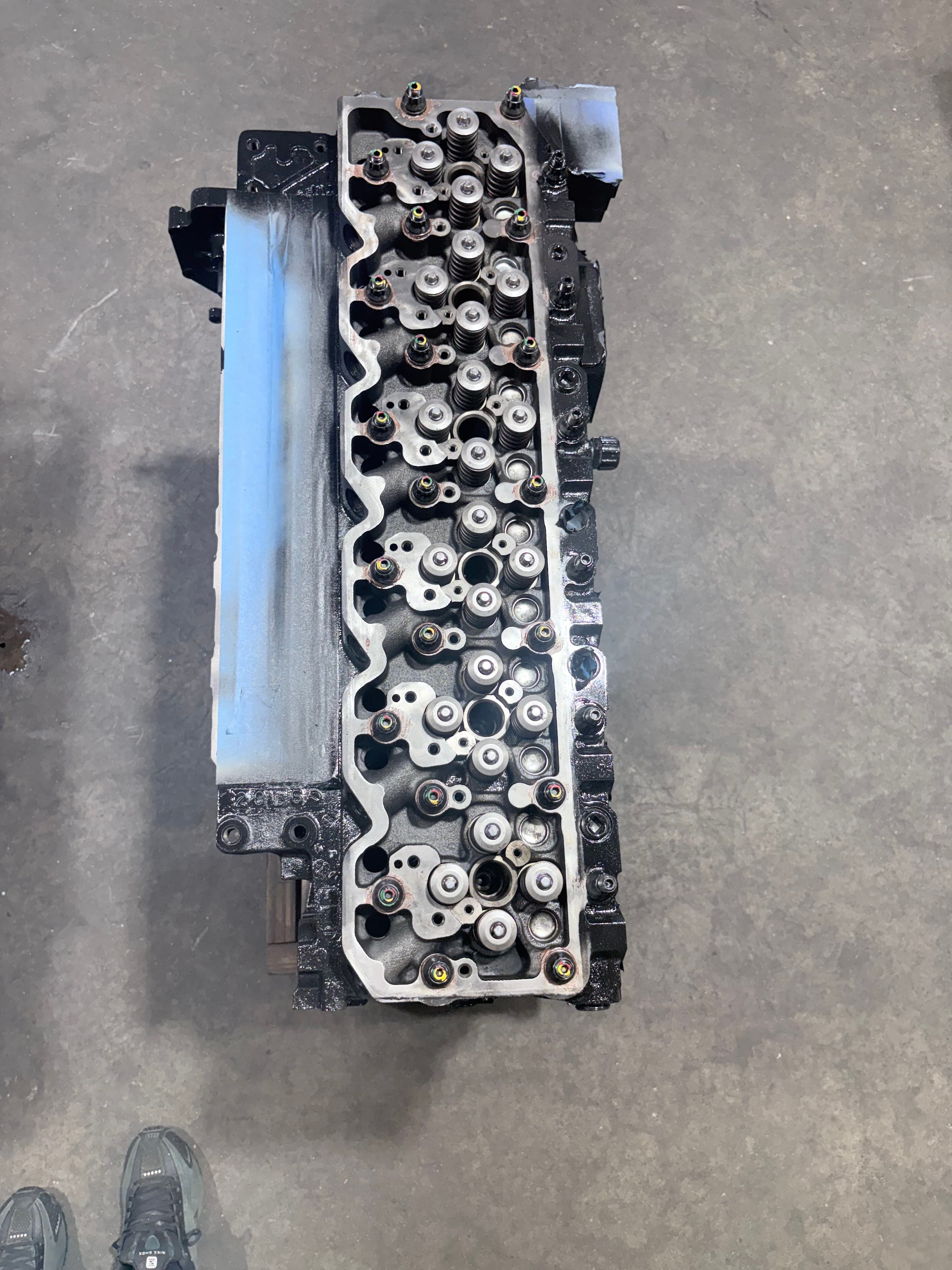 Top-down view of a black and silver engine cylinder head on a concrete floor.
