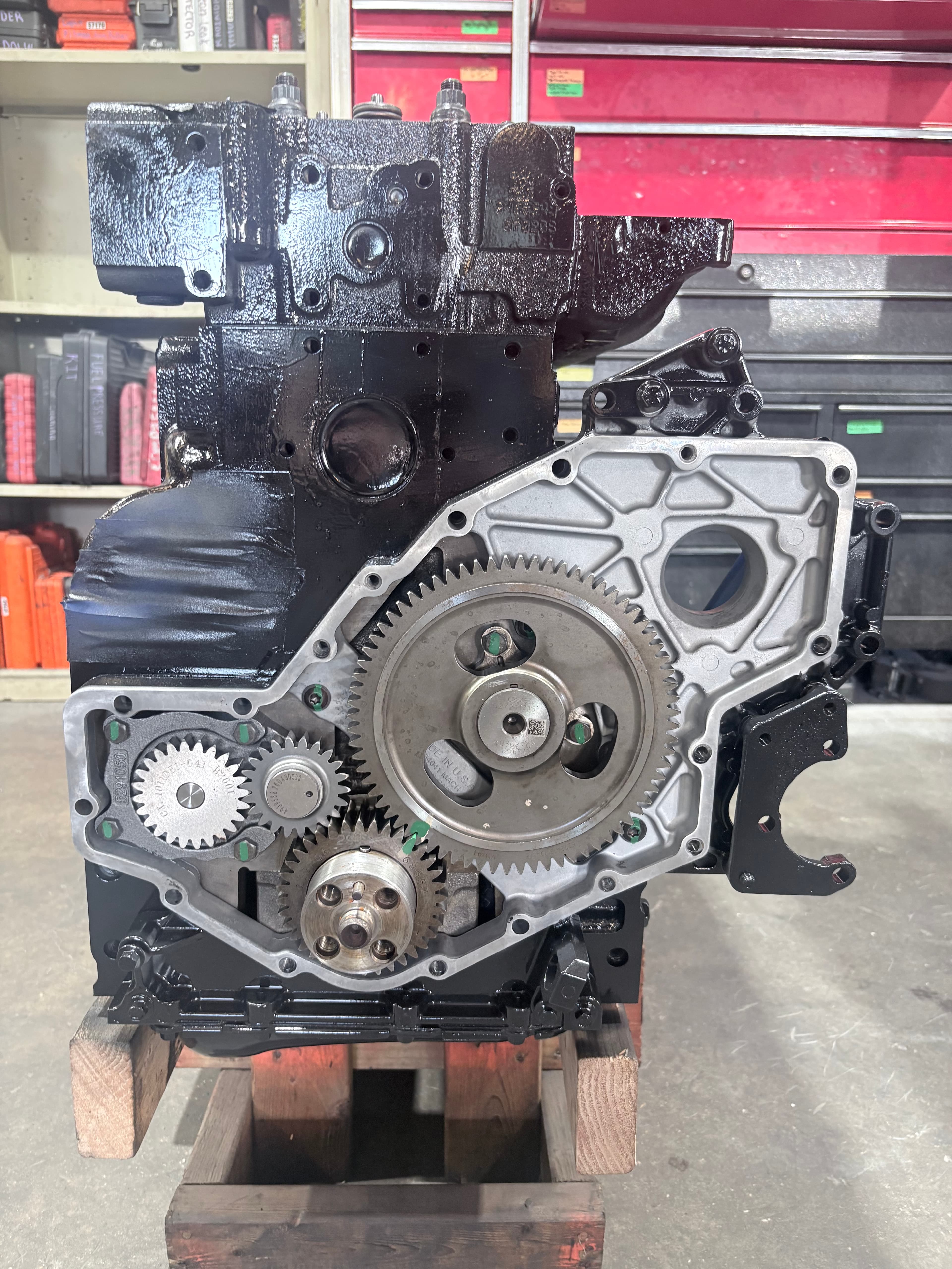 Glossy black diesel engine block with exposed timing gears on a wooden workshop stand.
