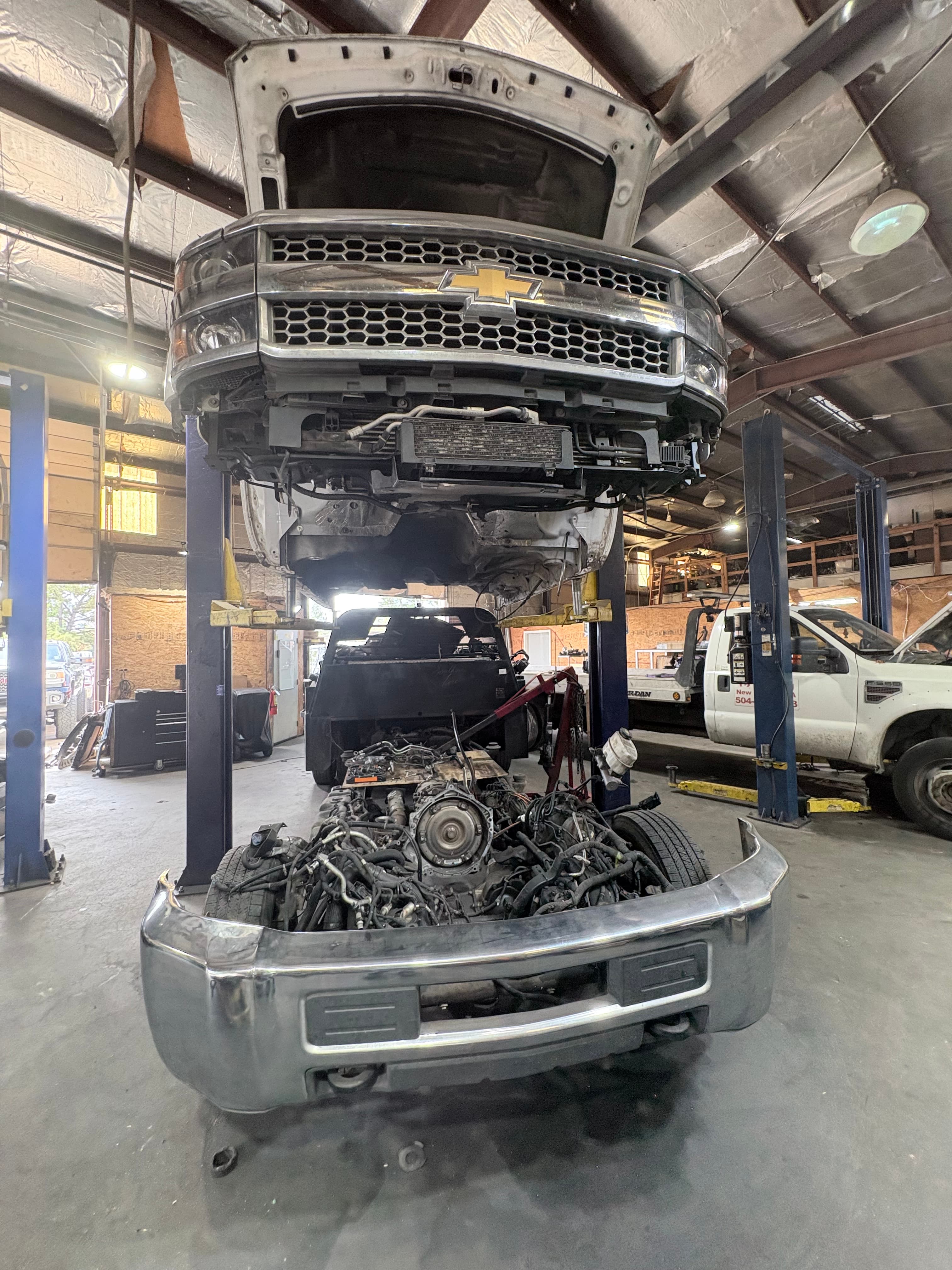 White Chevrolet truck body lifted on a hoist above its exposed engine and chassis.