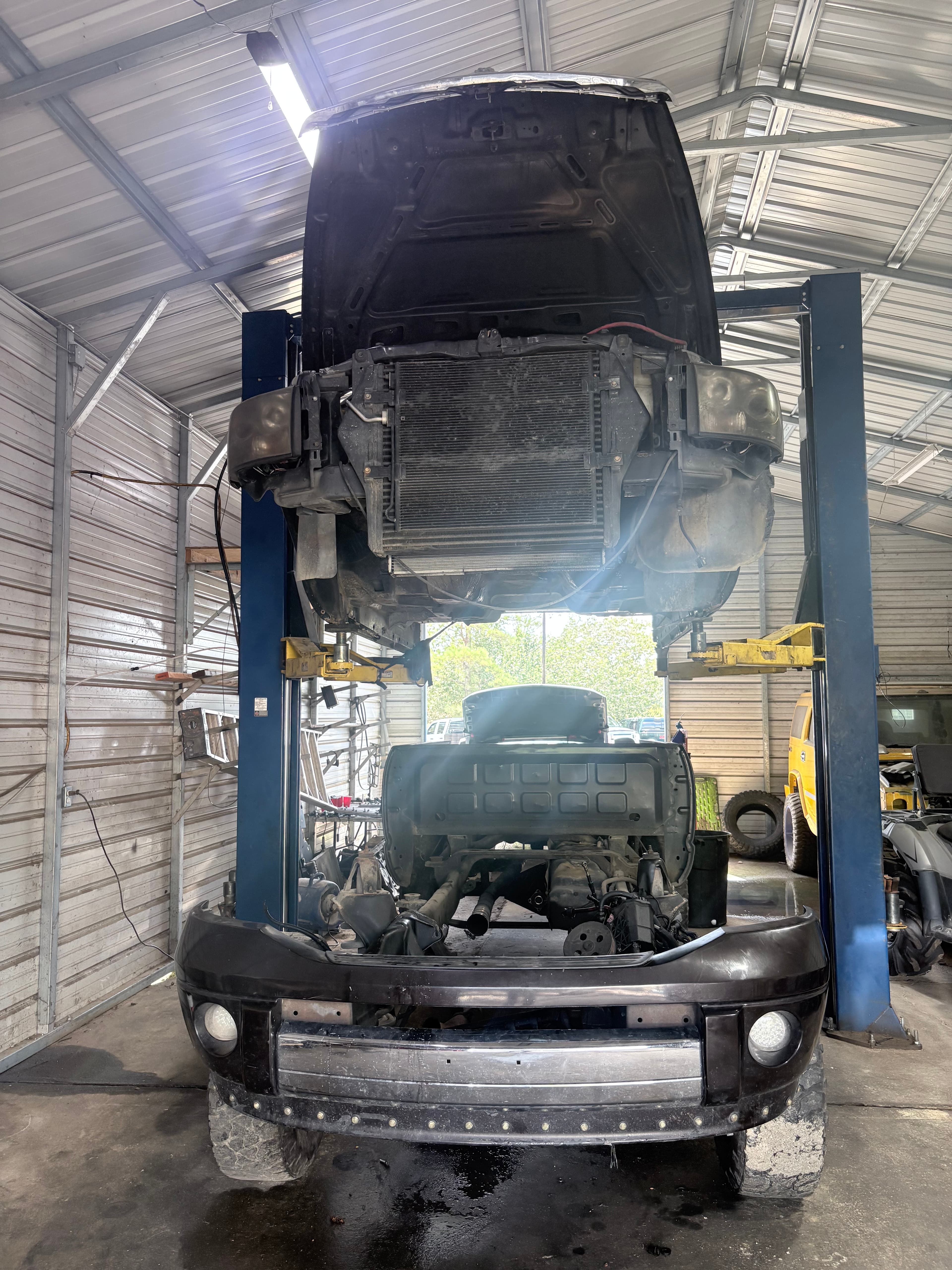 Black truck body raised on a hydraulic lift in a garage, separated from its chassis.