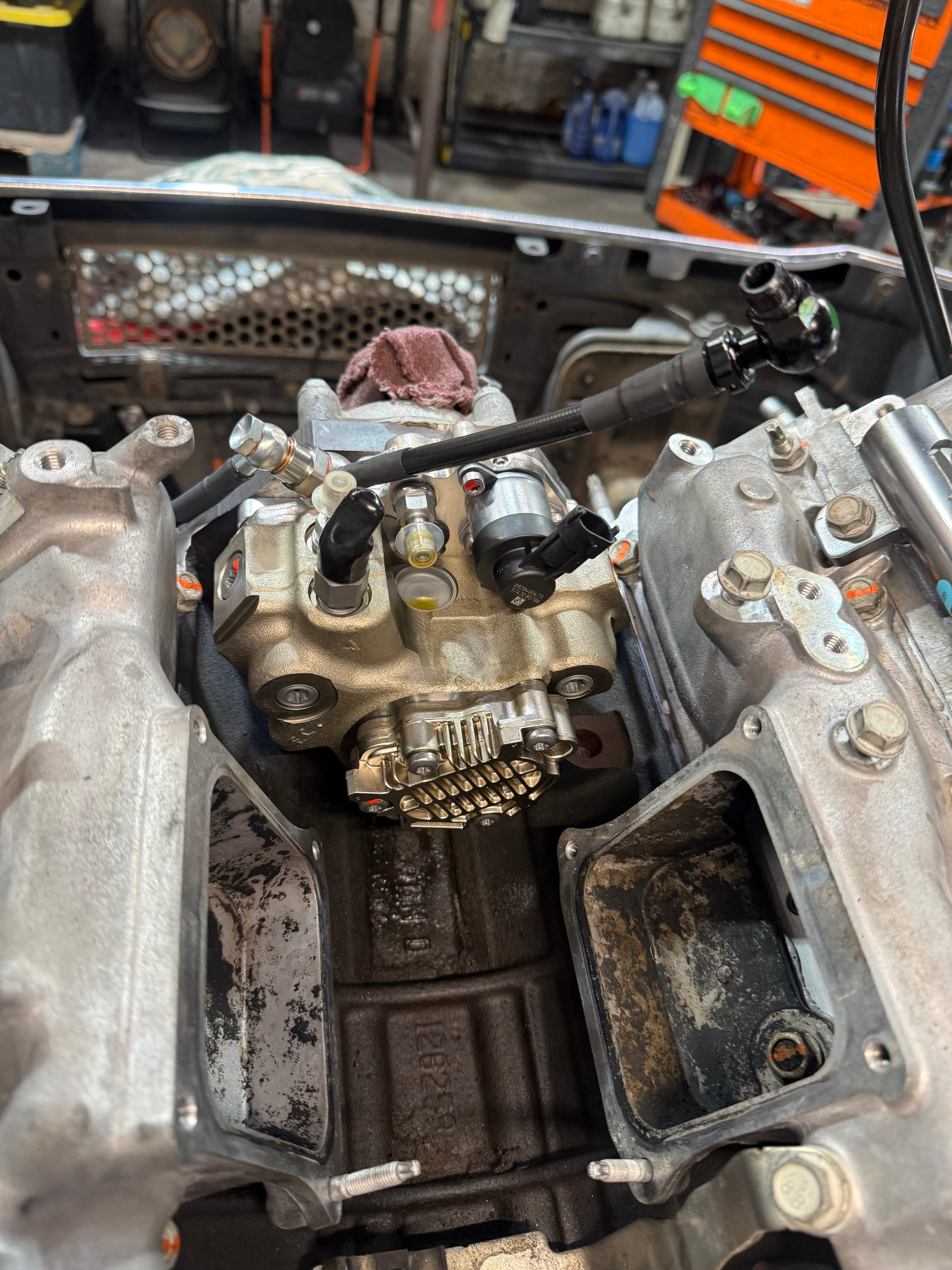 High-pressure fuel pump installed between intake manifold runners in a vehicle's engine compartment.