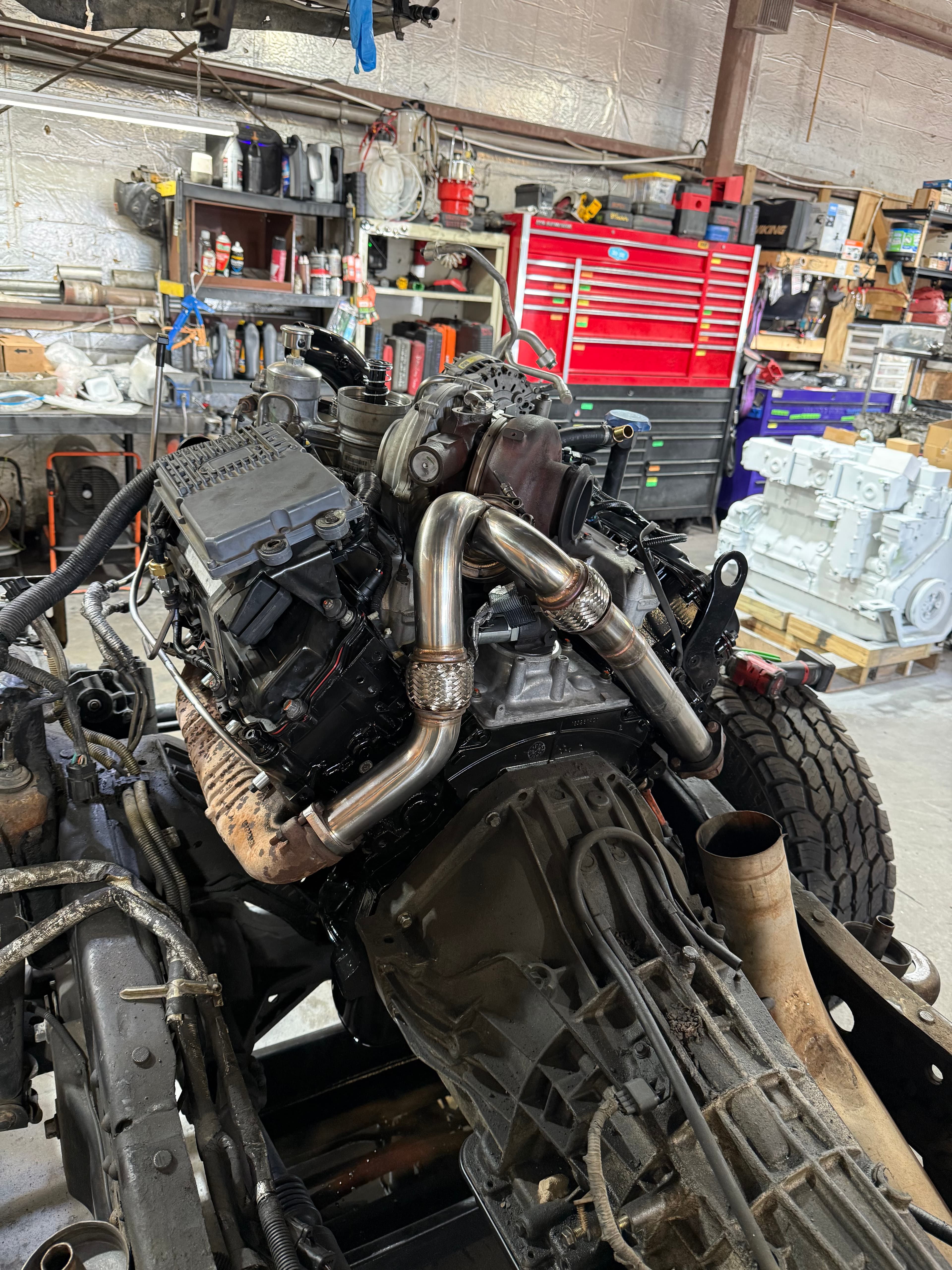 Large truck engine with polished silver exhaust pipes in a workshop with a red toolbox.