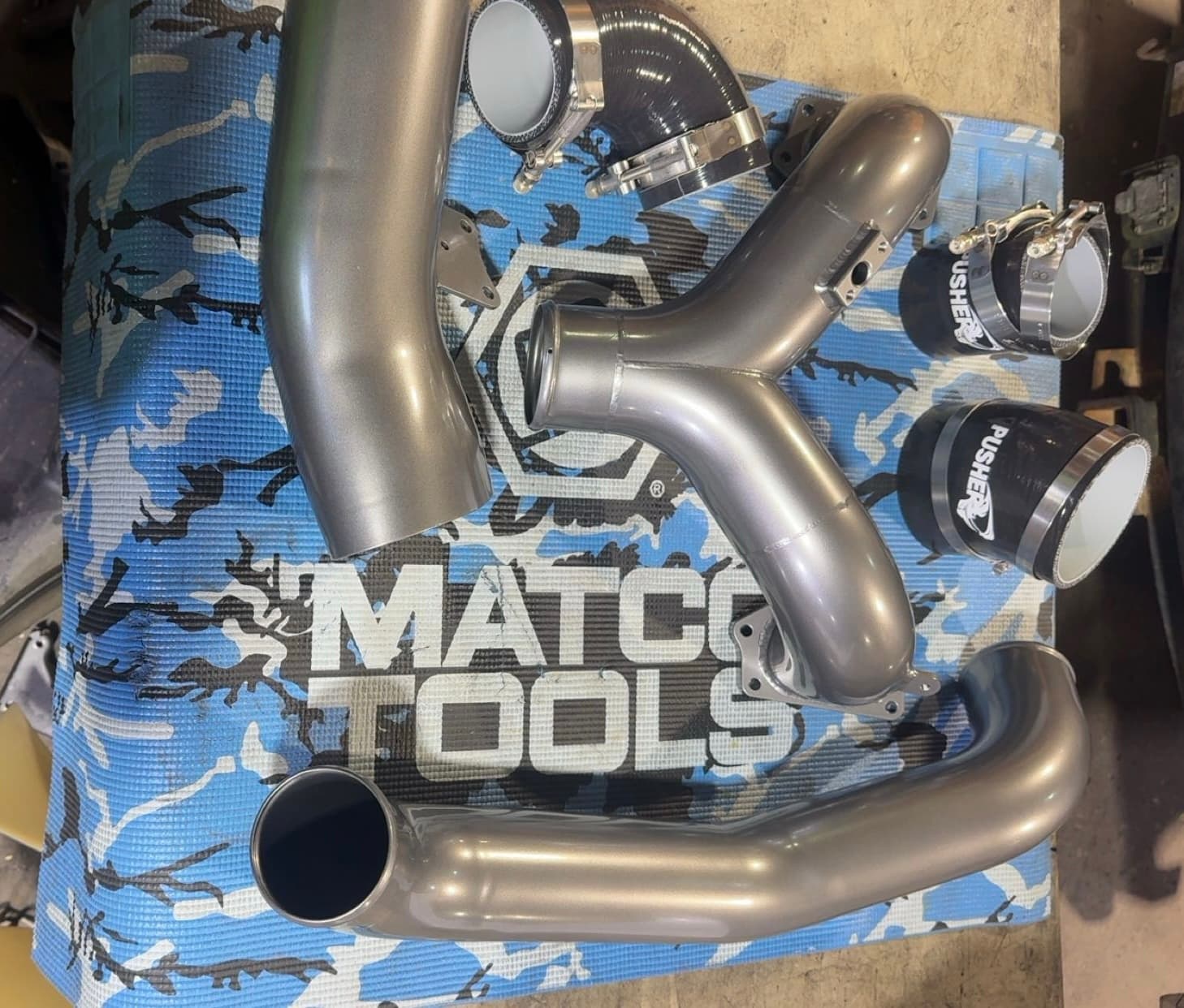 Metallic grey intake pipes and black couplers arranged on a blue Matco Tools mat.