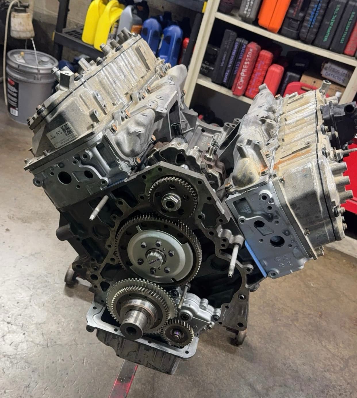 Large V-engine with exposed front timing gears mounted on a stand in a workshop setting.