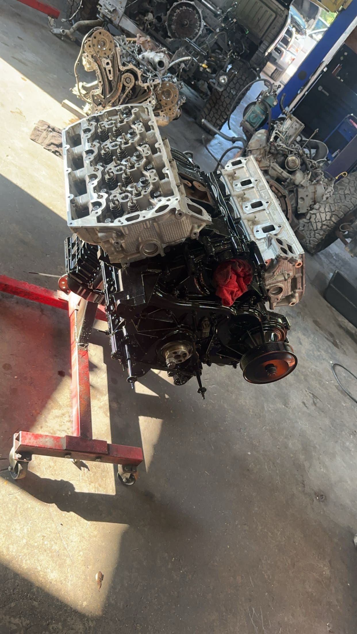 Black engine block with silver cylinder heads on a red engine stand in a garage.