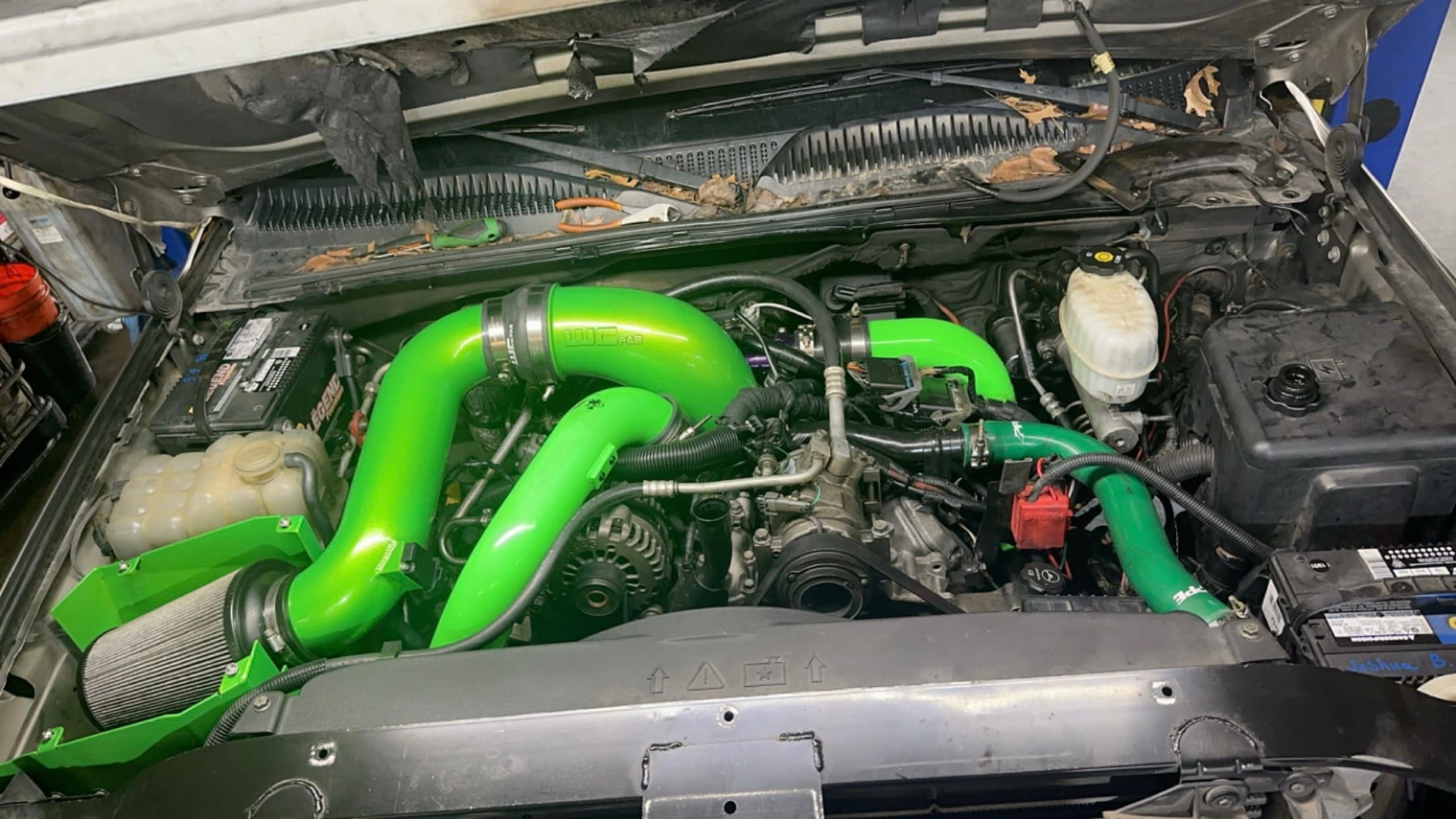 Vehicle engine bay featuring vibrant lime green aftermarket intake pipes and a performance air filter.