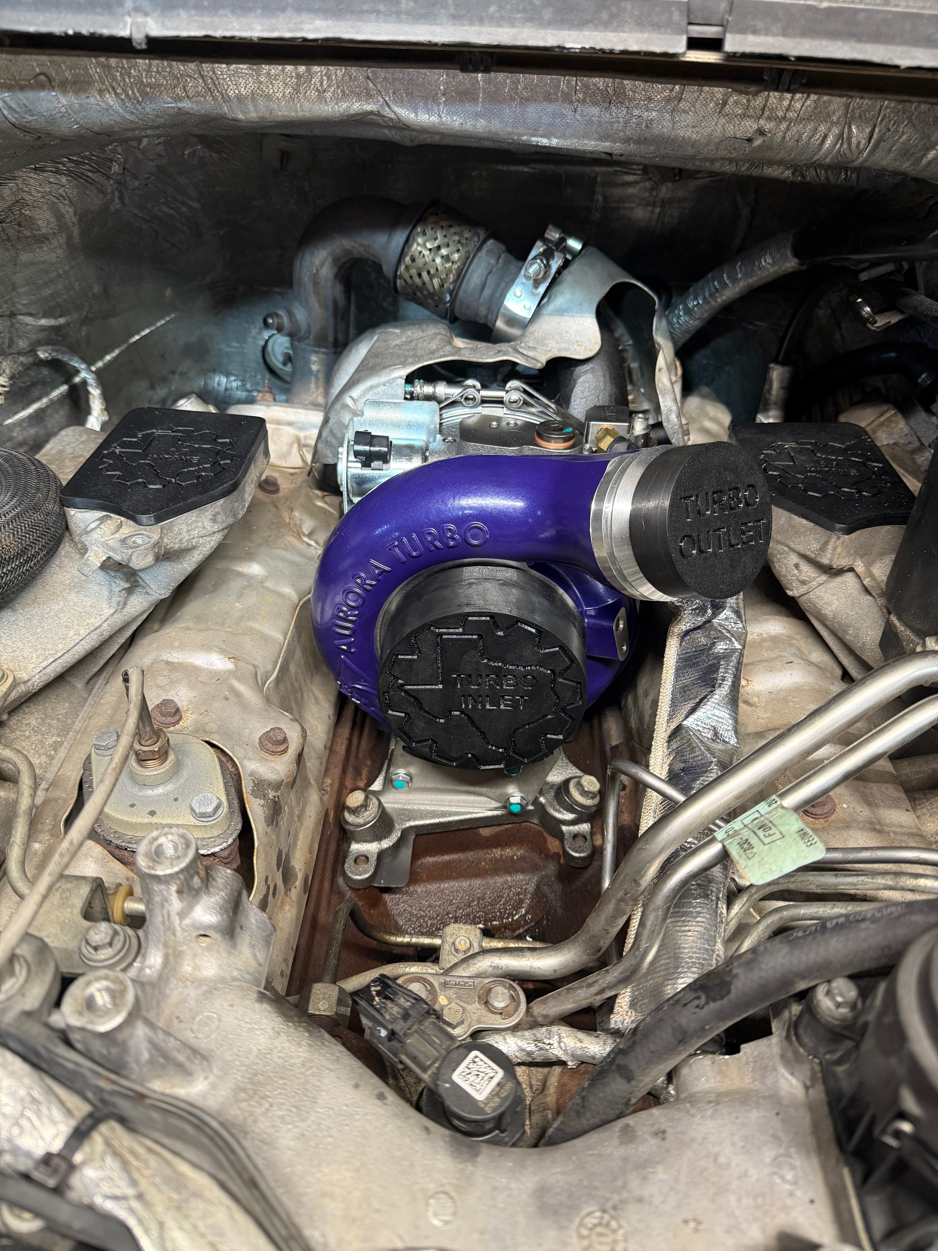 Purple Aurora Turbo with black inlet and outlet caps installed in a vehicle engine bay.